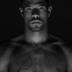 modello nero con sguardo intenso e tatuaggi sul petto