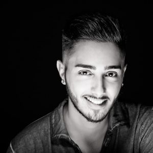 ragazzo con occhi a mandorla, sorriso divertito, barba e baffi corti e capelli a spazzola