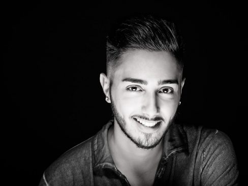 ragazzo con occhi a mandorla, sorriso divertito, barba e baffi corti e capelli a spazzola